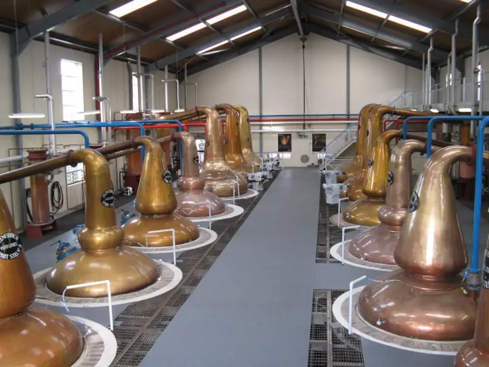 Una fila di distillatori in acciaio dorato allineati in una distilleria scozzese.