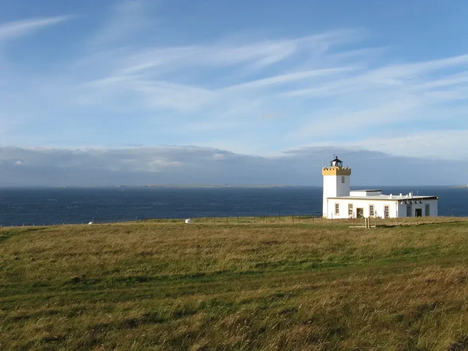 Un faro bianco si staglia su un paesaggio costiero scozzese erboso.
