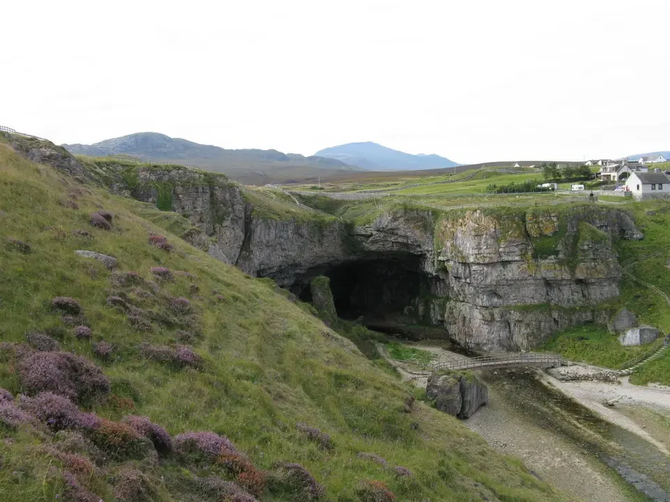 Una formazione rocciosa con un arco naturale attraversa un paesaggio collinare scozzese.