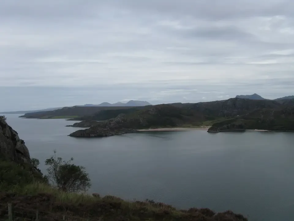 Paesaggio costiero scozzese con isole e colline sotto un cielo coperto.