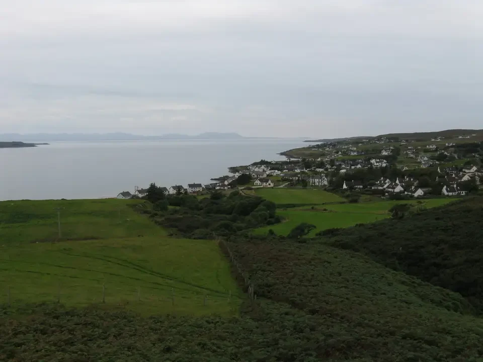 Paesaggio costiero verde e ondulato della Scozia con insediamenti lungo la riva.