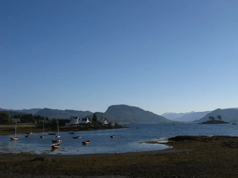 Paesaggio lacustre con case e barche in Scozia sotto un cielo sereno.
