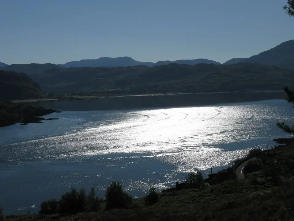 Un corpo d'acqua illuminato riflette sulle colline ondulate della Scozia.