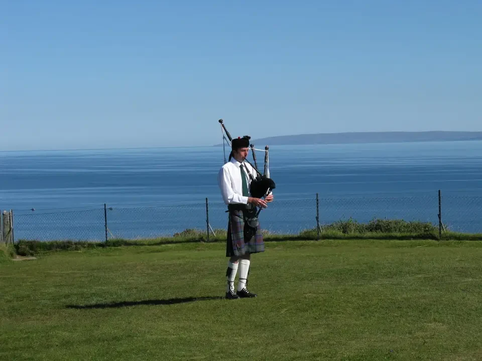 Un uomo indossa un kilt e sta in piedi su un prato di fronte al mare.