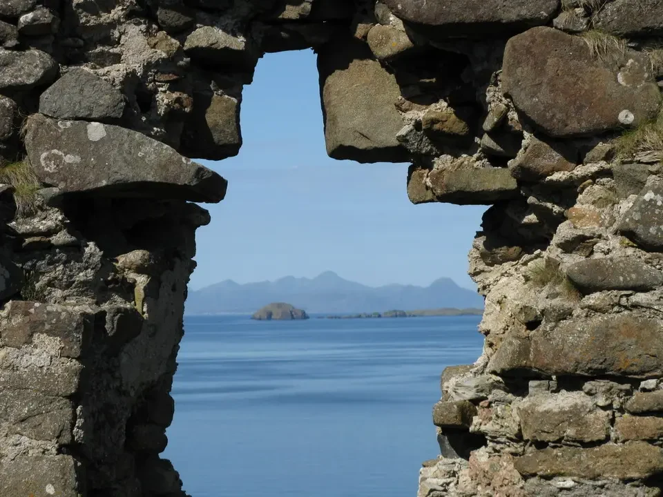 Vista panoramica del paesaggio marino e delle isole della Scozia attraverso una struttura in pietra antica.