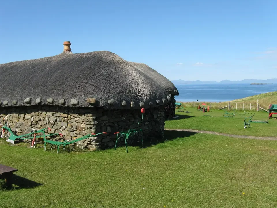 Una vecchia casa in pietra con tetto di paglia si trova su un prato verde vicino al mare in Scozia.