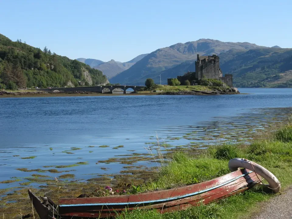 Castello su un'isola nel paesaggio scozzese con un ponte e una barca in primo piano.