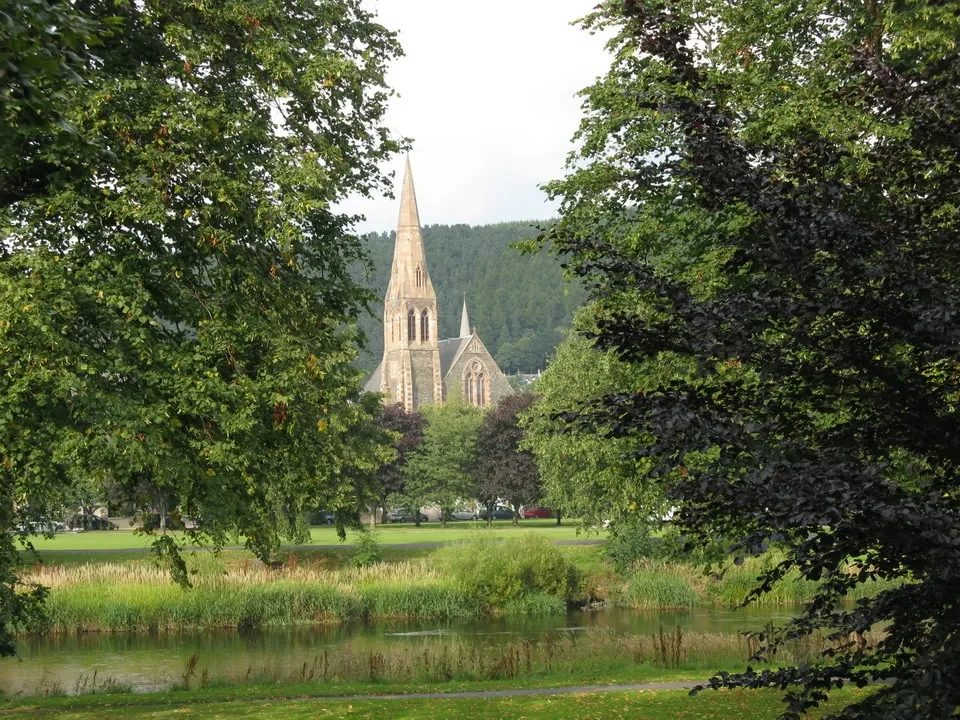 Vista panoramica di una chiesa in pietra incorniciata da alberi e un corpo d'acqua scozzese.