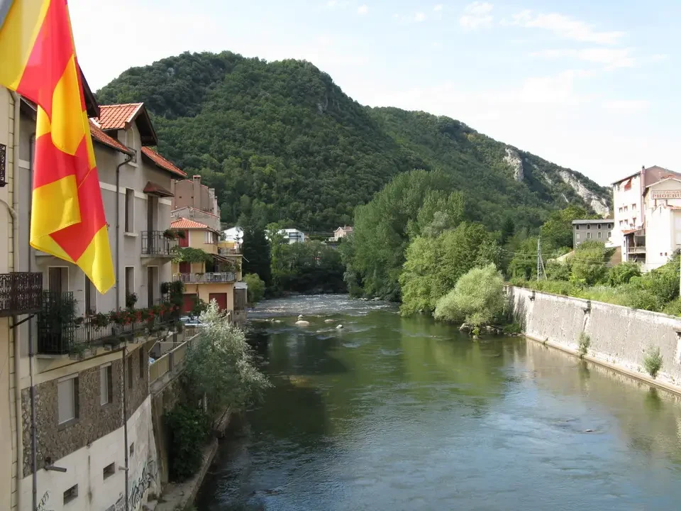 Un fiume scorre tra le colline boscose con edifici lungo la riva.