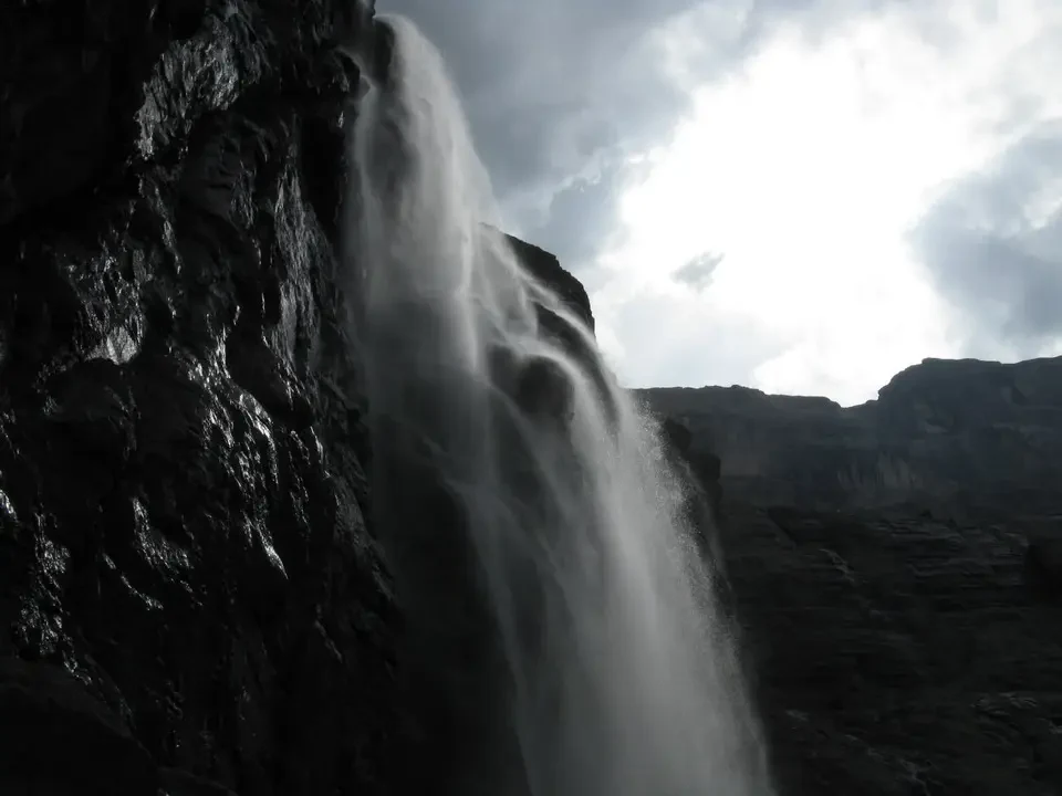 Una cascata imponente scende su una parete rocciosa sotto un cielo nuvoloso.
