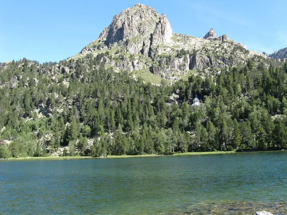 Lago alpino con montagne rocciose e foreste boscose ai piedi.
