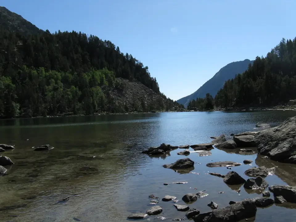 Un lago alpino circondato da montagne boscose e rocciose.