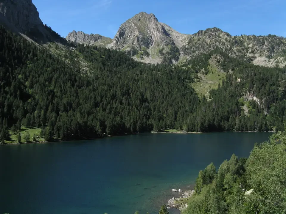Un lago alpino circondato da montagne boscose e rocciose.