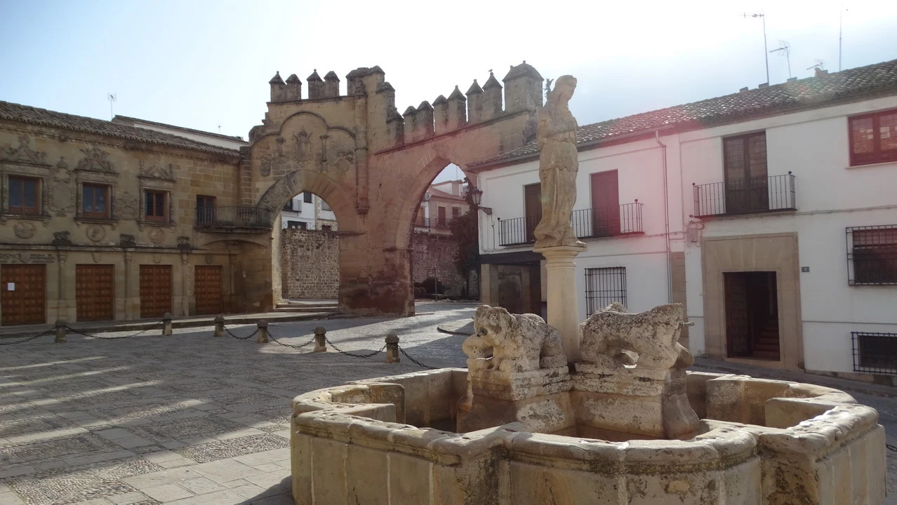 Una piazza con un arco in pietra e una fontana in primo piano in Andalusia o Algarve.