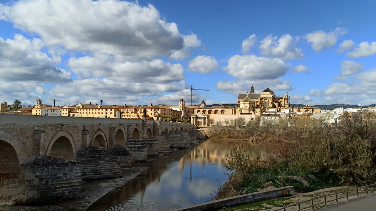 Un ponte romano attraversa un fiume con edifici storici in Andalusia o Algarve.