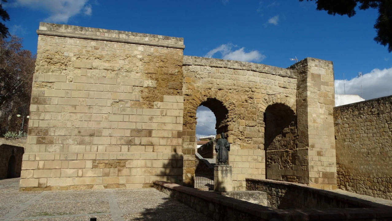 Porta romana in pietra con archi in un paesaggio andaluso.