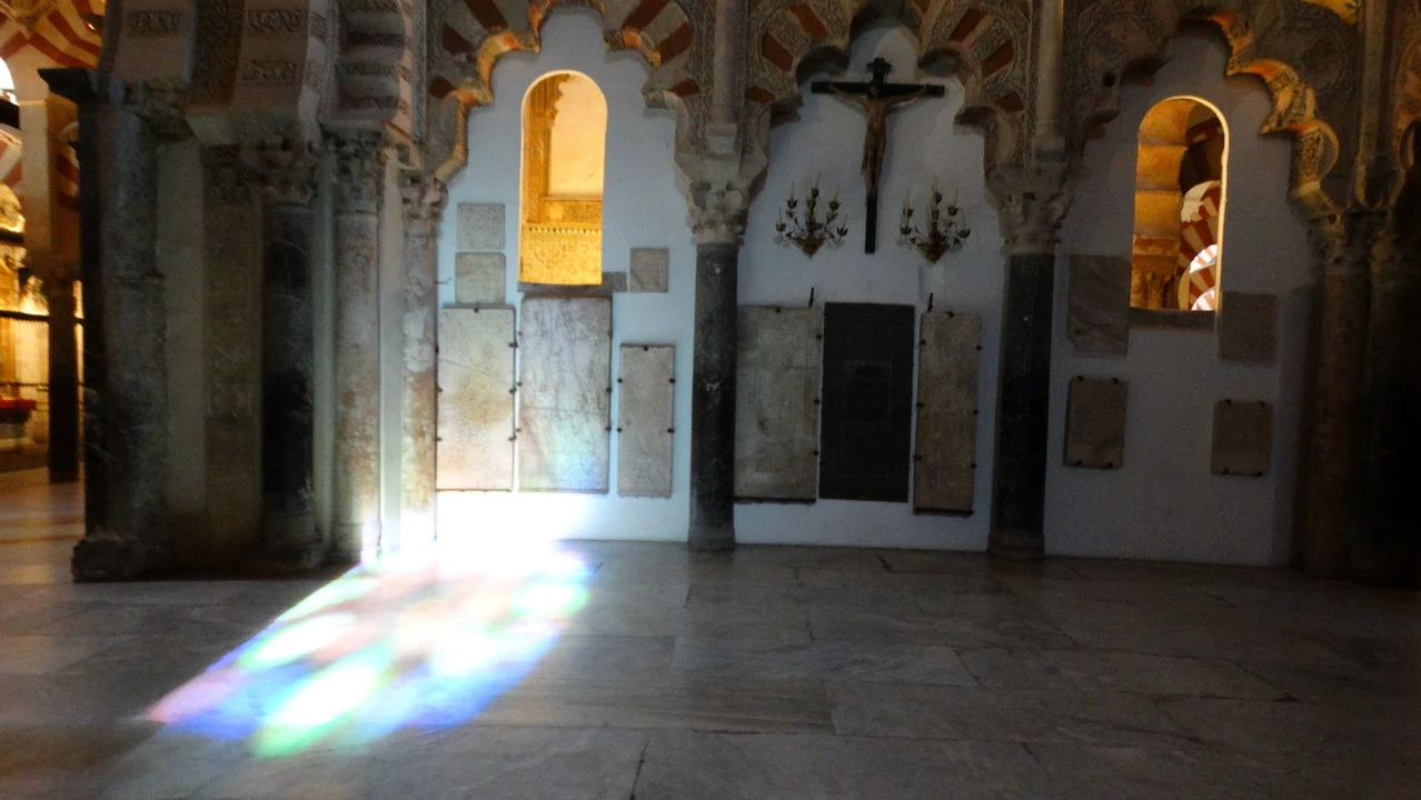 Interno della Mezquita di Cordova con archi decorati e luce che entra dalle aperture.