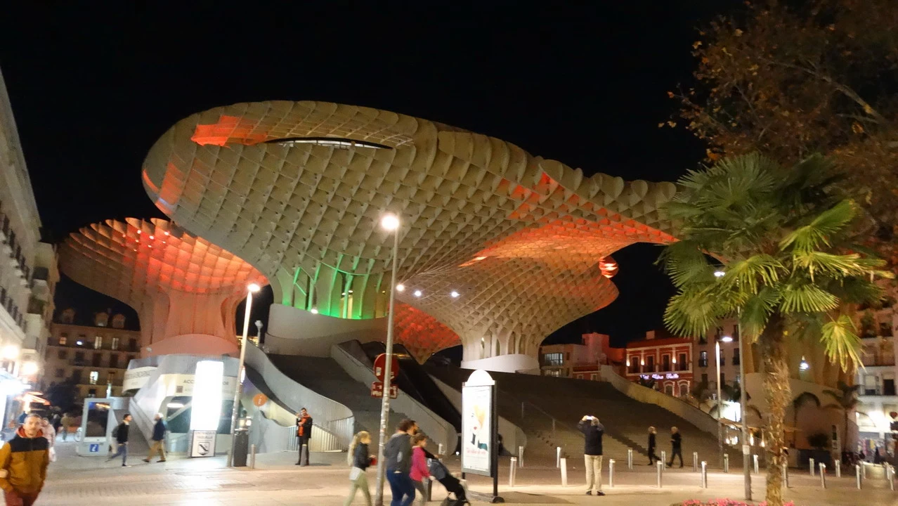 Architettura moderna illuminata di un edificio con forma a conchiglia in una piazza serale.