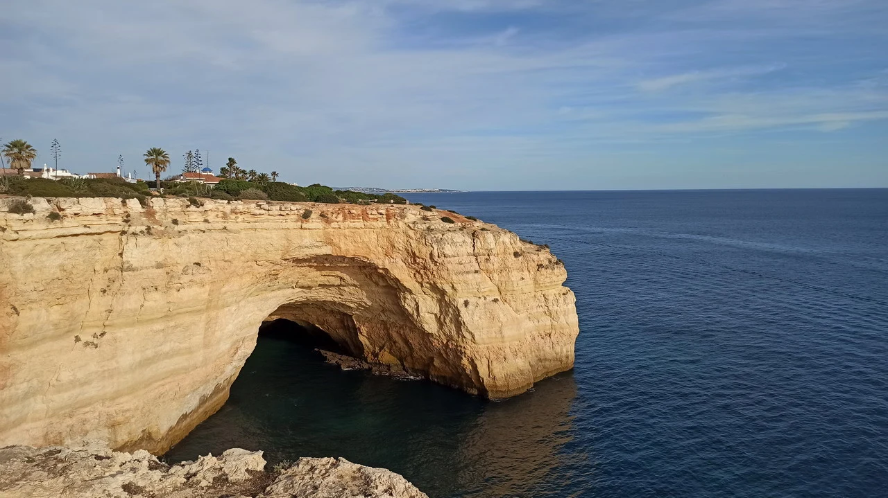 Un arco naturale nella scogliera costiera si apre sul mare blu.