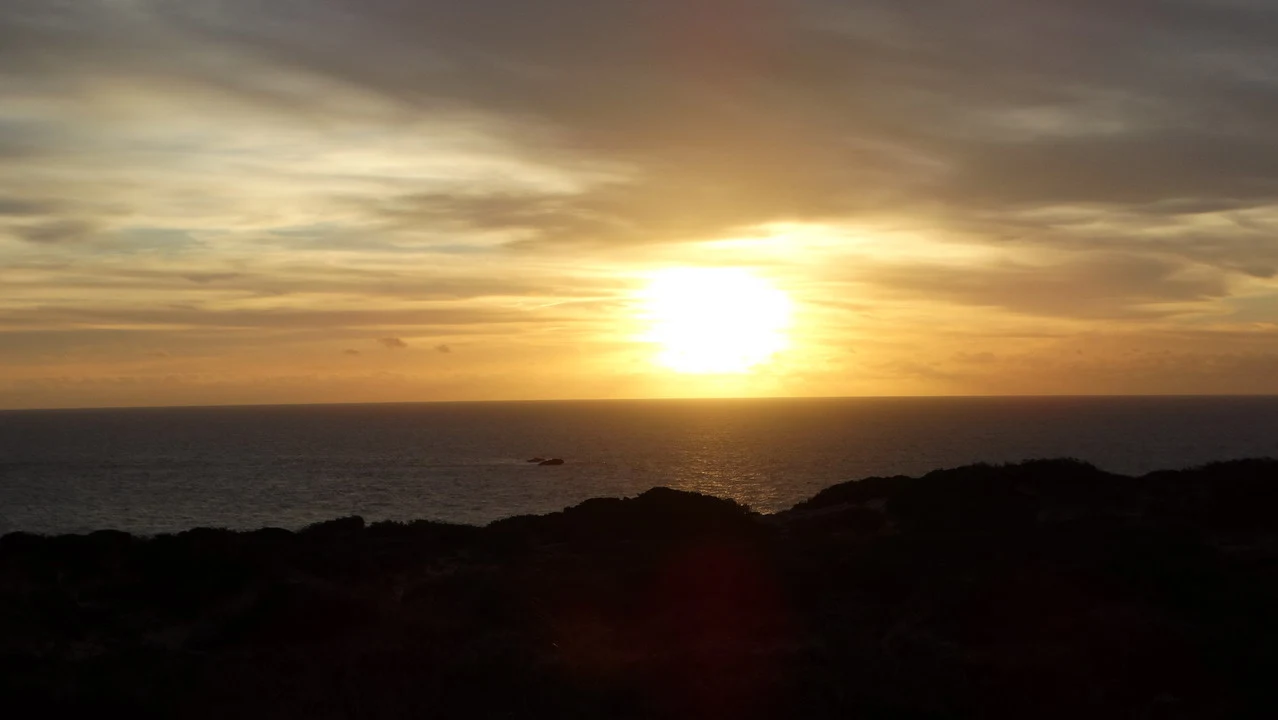 Tramonto dorato sul mare dell'Algarve con silhouette costiere scure.