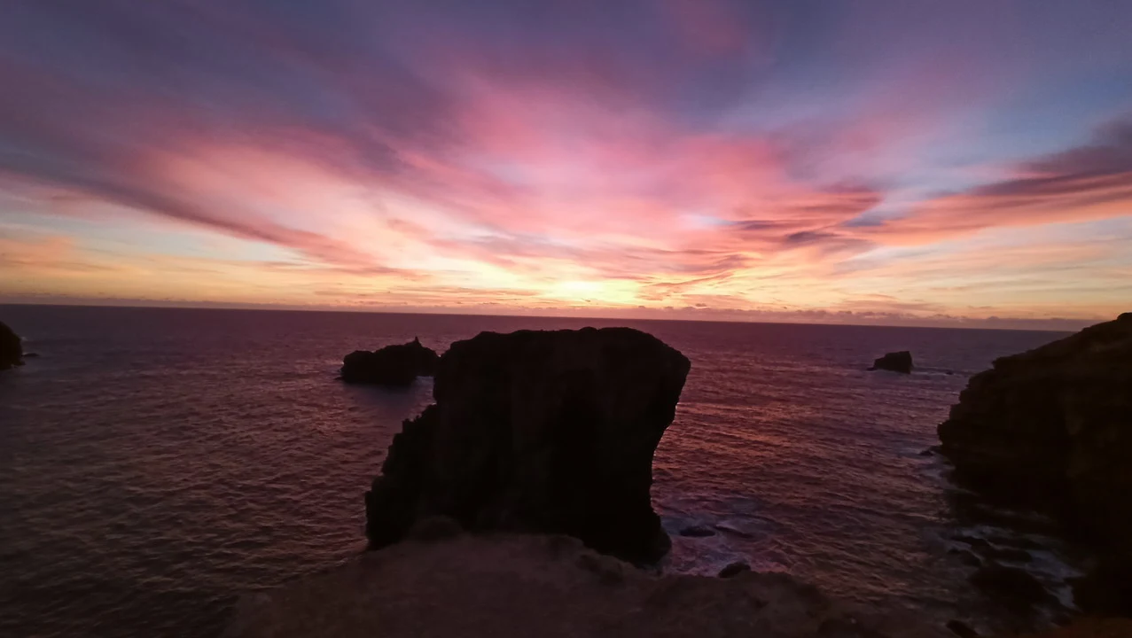 Tramonto spettacolare sul mare con nuvole rosse e arancioni sopra le scogliere.