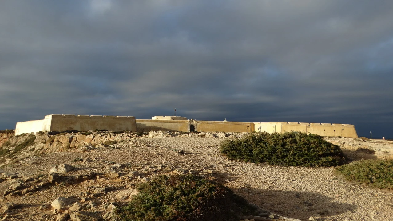Mura di pietra che si estendono lungo una costa rocciosa sotto un cielo nuvoloso.