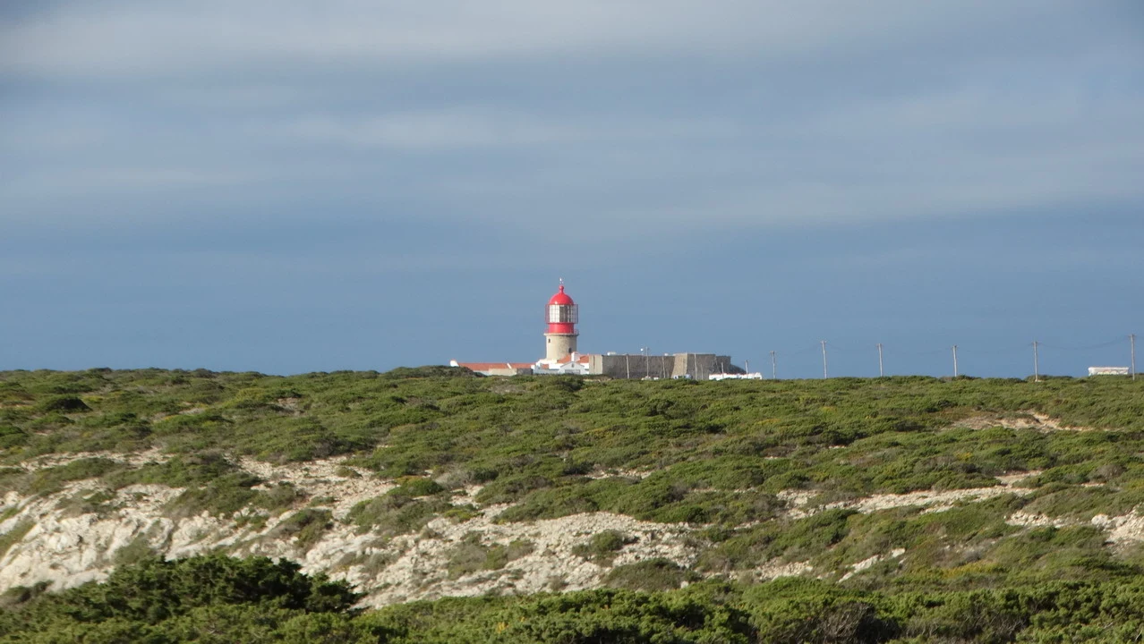 Un faro si staglia sopra un paesaggio costiero mediterraneo.