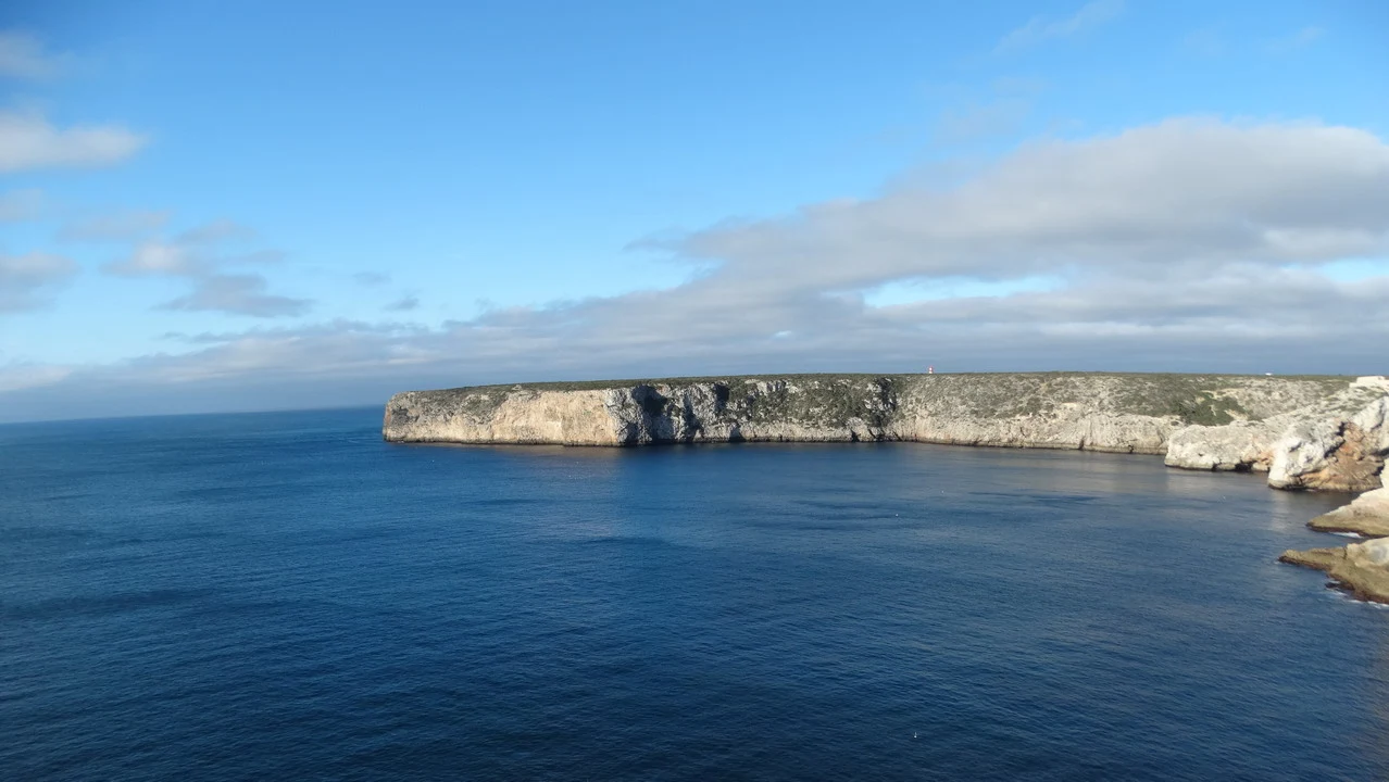 Una scogliera rocciosa si estende lungo la costa sotto un cielo sereno.