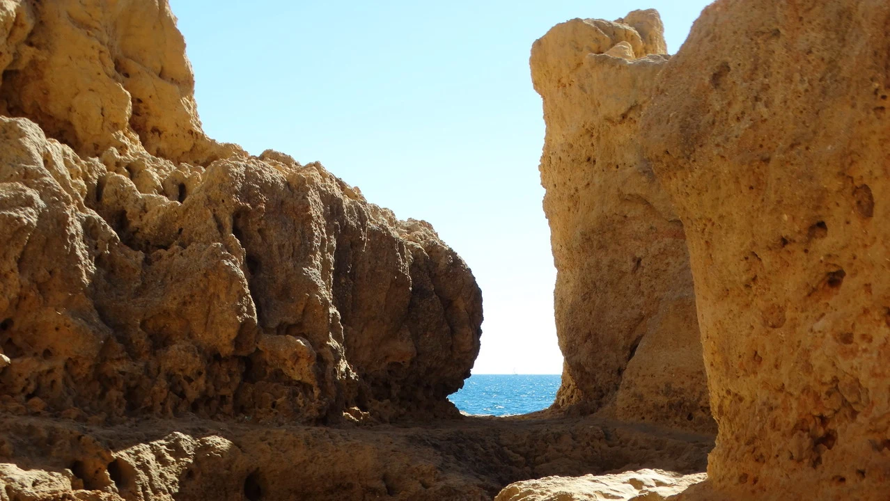 Formazioni rocciose dorate costeggiano il mare in una scogliera soleggiata.