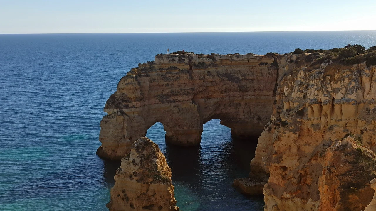 Una formazione rocciosa costiera si protende verso il mare con archi naturali.