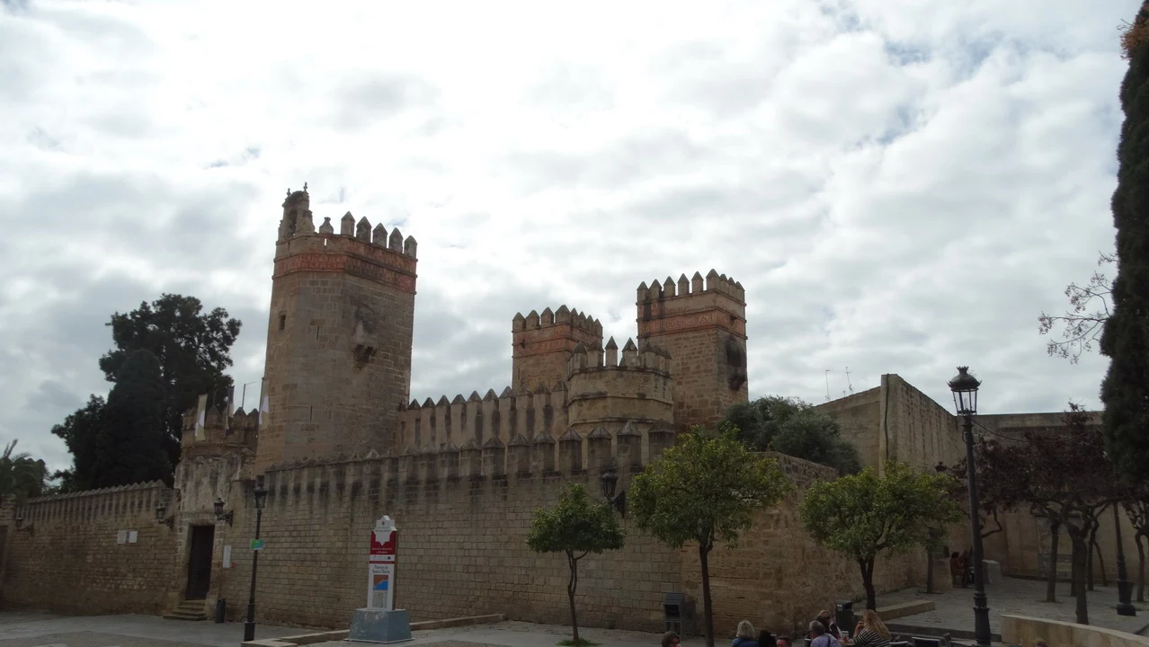 Mura fortificate di un castello in pietra con merlature sotto un cielo nuvoloso.
