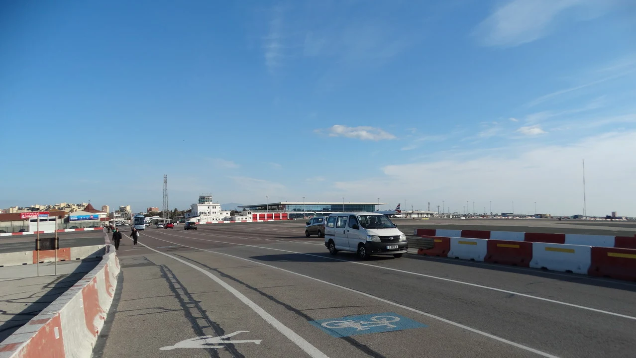 Un aeroporto è visibile con una strada di accesso e veicoli in primo piano.