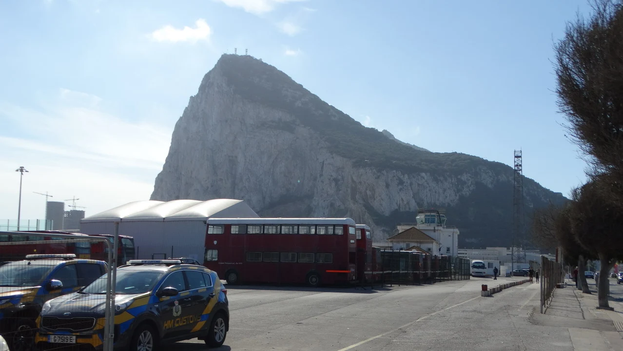 Un autobus rosso si trova davanti a una formazione rocciosa imponente in un contesto di viaggio tra Andalusia e Algarve.