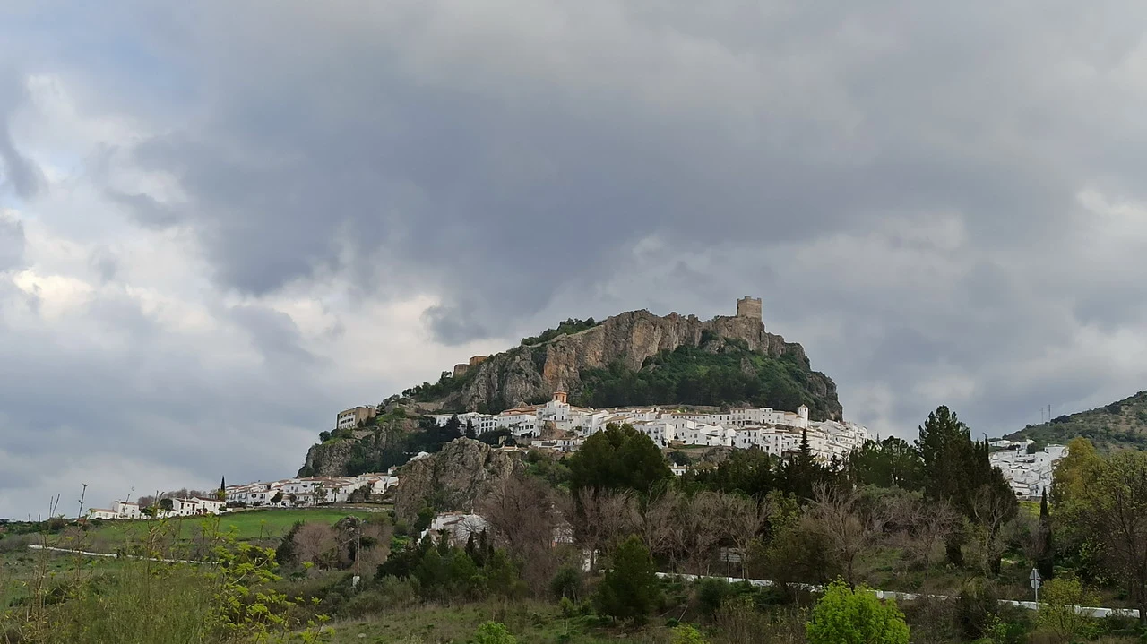 Un villaggio bianco si staglia su una collina rocciosa sotto un cielo nuvoloso in Andalusia.