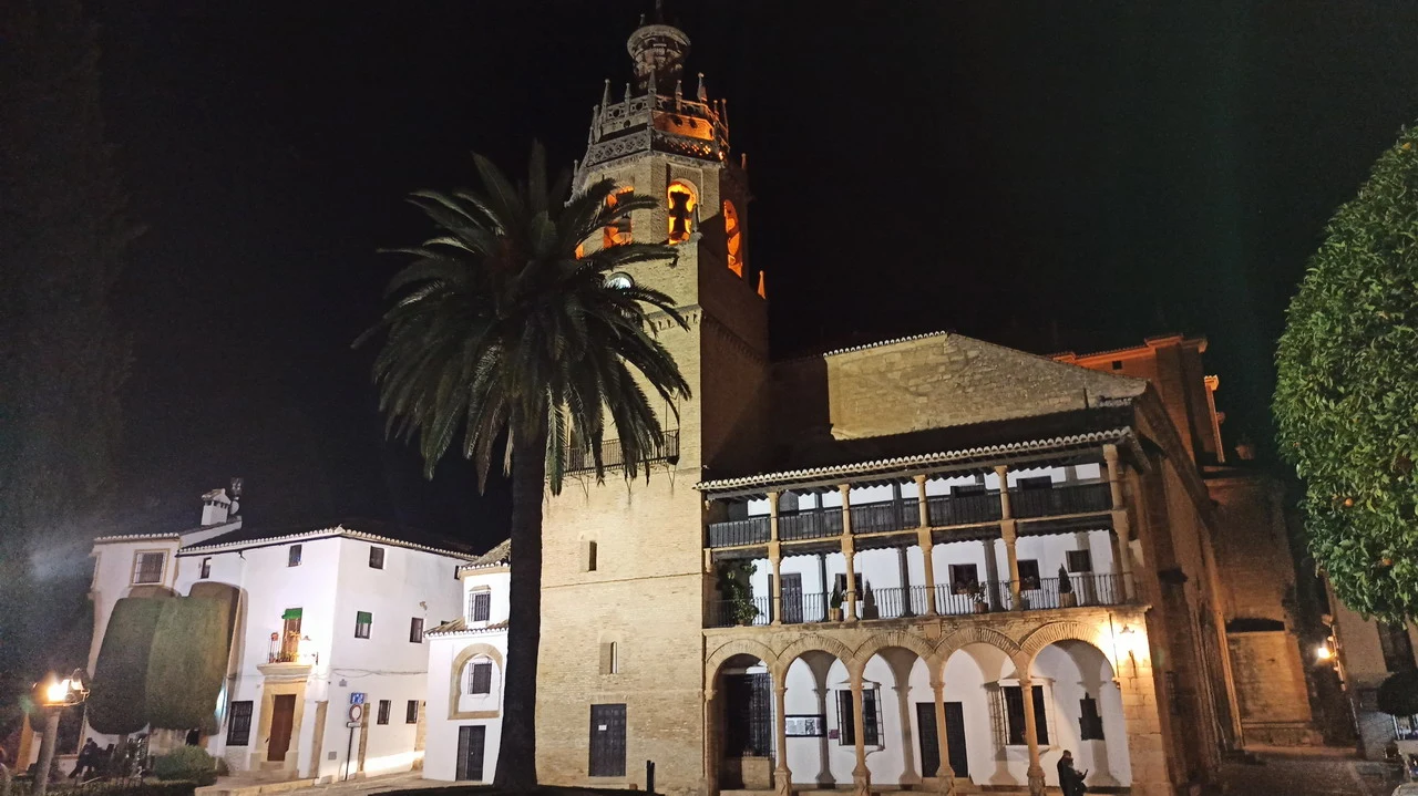 Vista notturna di un edificio storico con torre in stile andaluso e palma in primo piano.