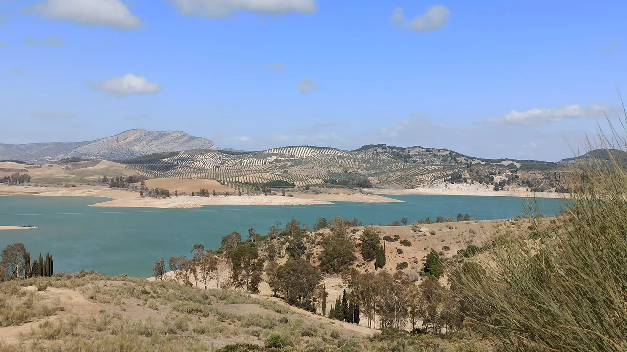 Paesaggio ampio che mostra un bacino d'acqua circondato da colline e vegetazione secca in Andalusia o Algarve.