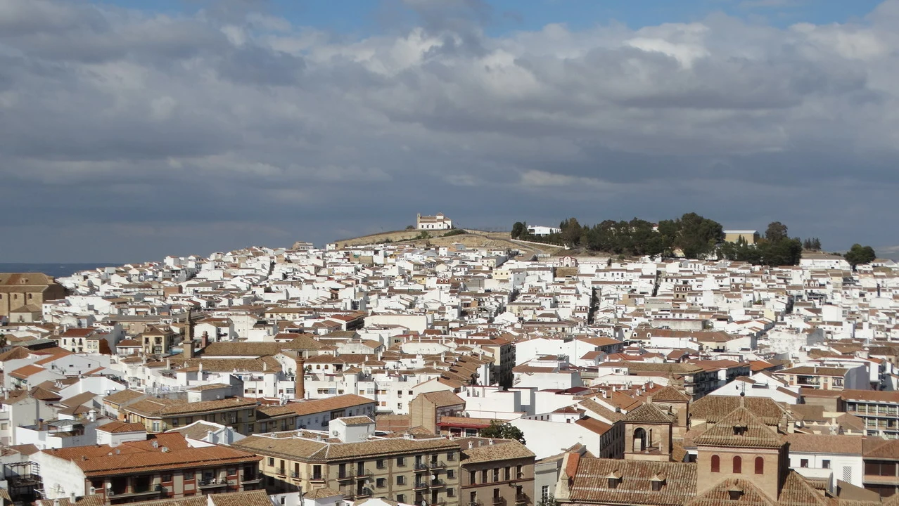 Vista panoramica di un paesaggio urbano e collinare con tetti in terracotta sotto un cielo nuvoloso.