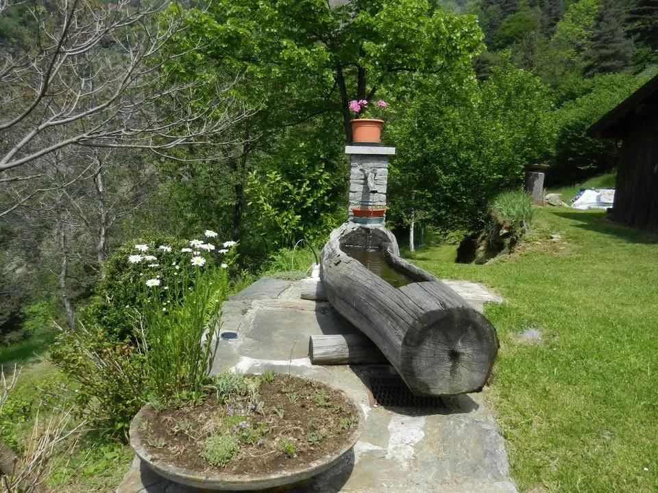 Una veduta esterna mostra un sentiero boschivo con elementi paesaggistici e giardini curati.