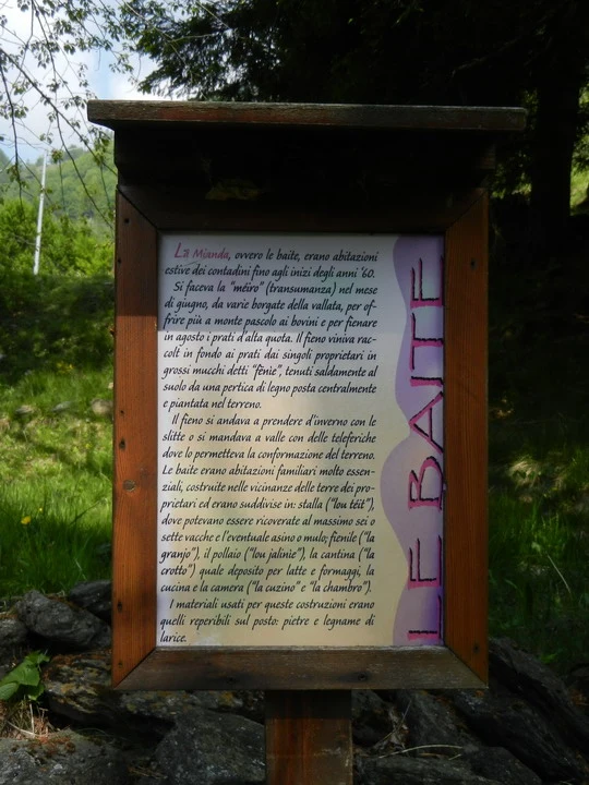 Segnaletica in legno lungo un sentiero boschivo indica informazioni sul percorso.