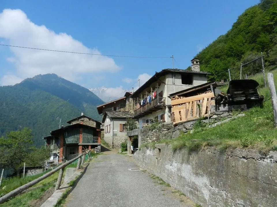 Una strada asfaltata costeggia un sentiero rurale con edifici in pietra in una valle montuosa.