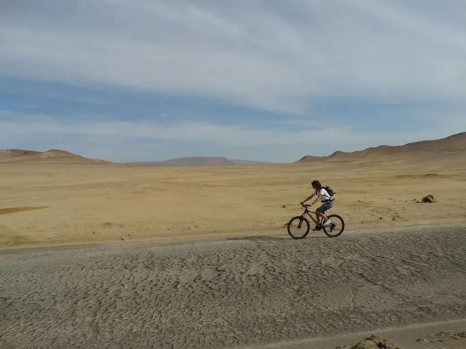 Una persona in bicicletta attraversa un vasto paesaggio desertico in Perù e Bolivia.