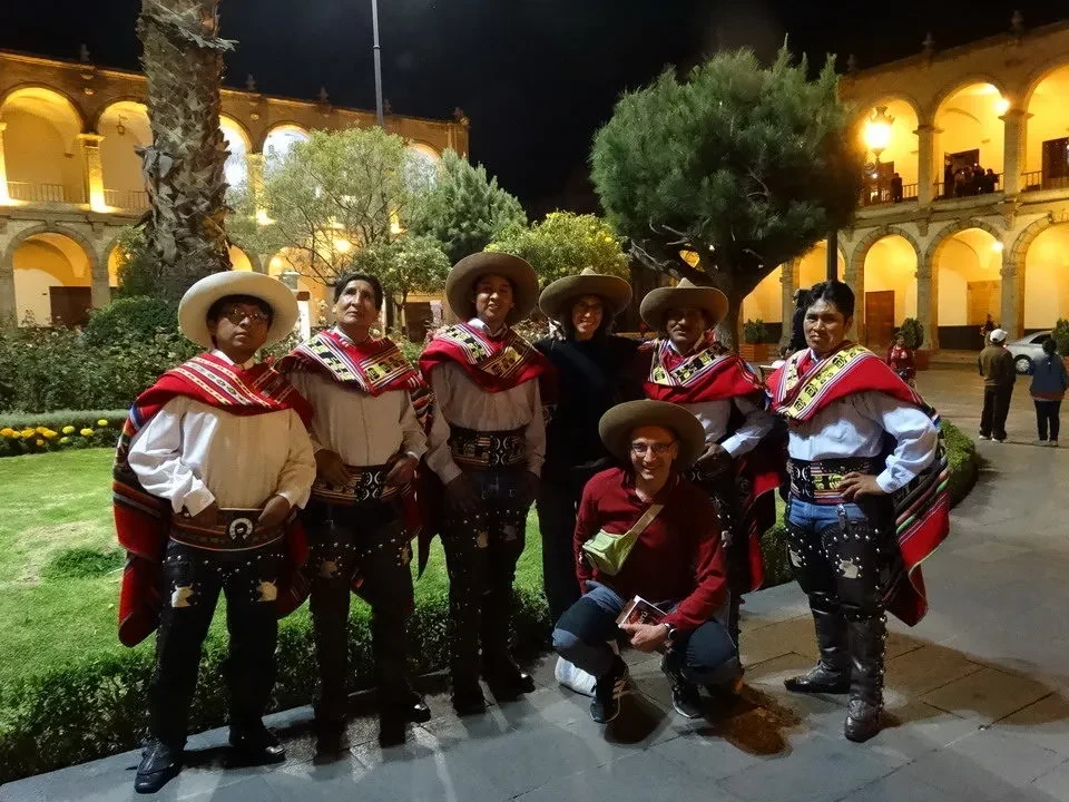 Uomini in costume tradizionale posano di fronte a un edificio storico al tramonto.