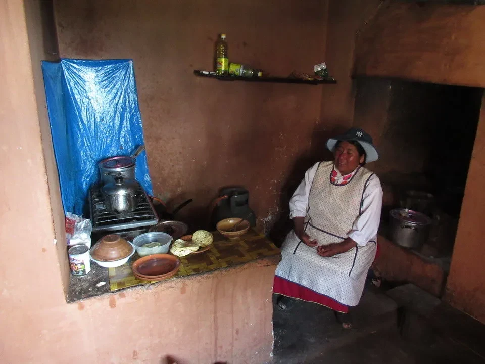 Una donna indiana è seduta davanti a una stufa in un ambiente rurale del Perù o della Bolivia.