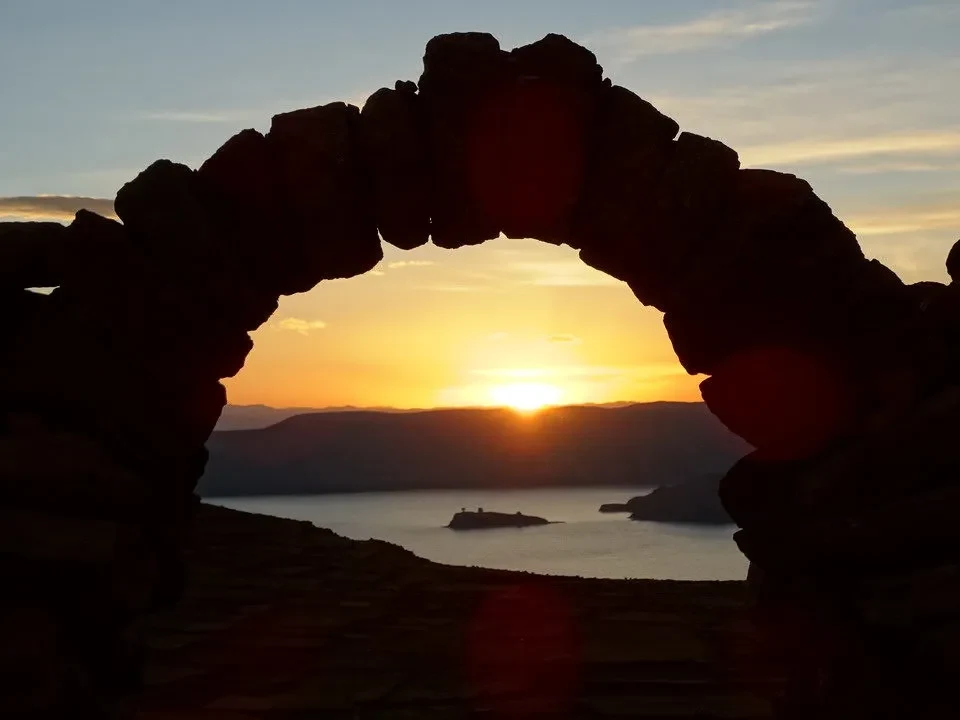 Tramonto sul lago alpino con un antico arco in pietra.