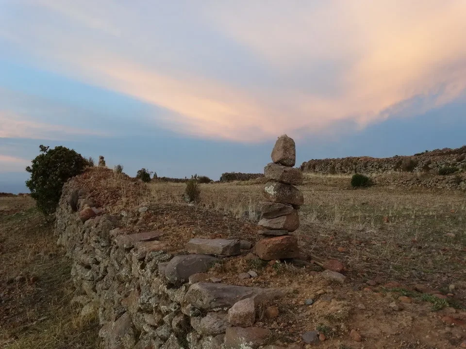 Resti di una struttura in pietra su un terreno arido con cielo al tramonto.