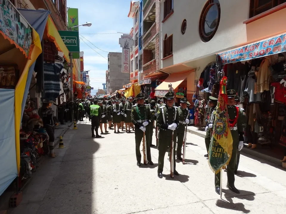 Una processione di soldati in uniforme cammina lungo una strada commerciale in Perù o Bolivia.
