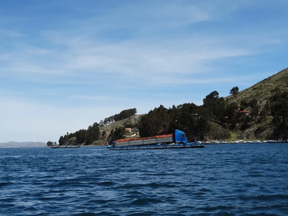 Un traghetto naviga attraverso l'acqua con una nave cargo in un paesaggio costiero.