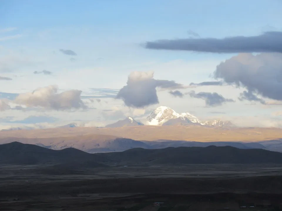 Paesaggio montano con cime innevate al tramonto sopra una pianura arida.