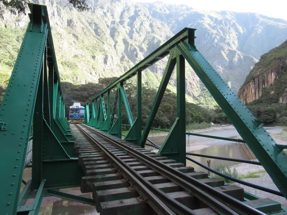 Ponte ferroviario in ferro che attraversa un fiume tra montagne verdi e ripide.