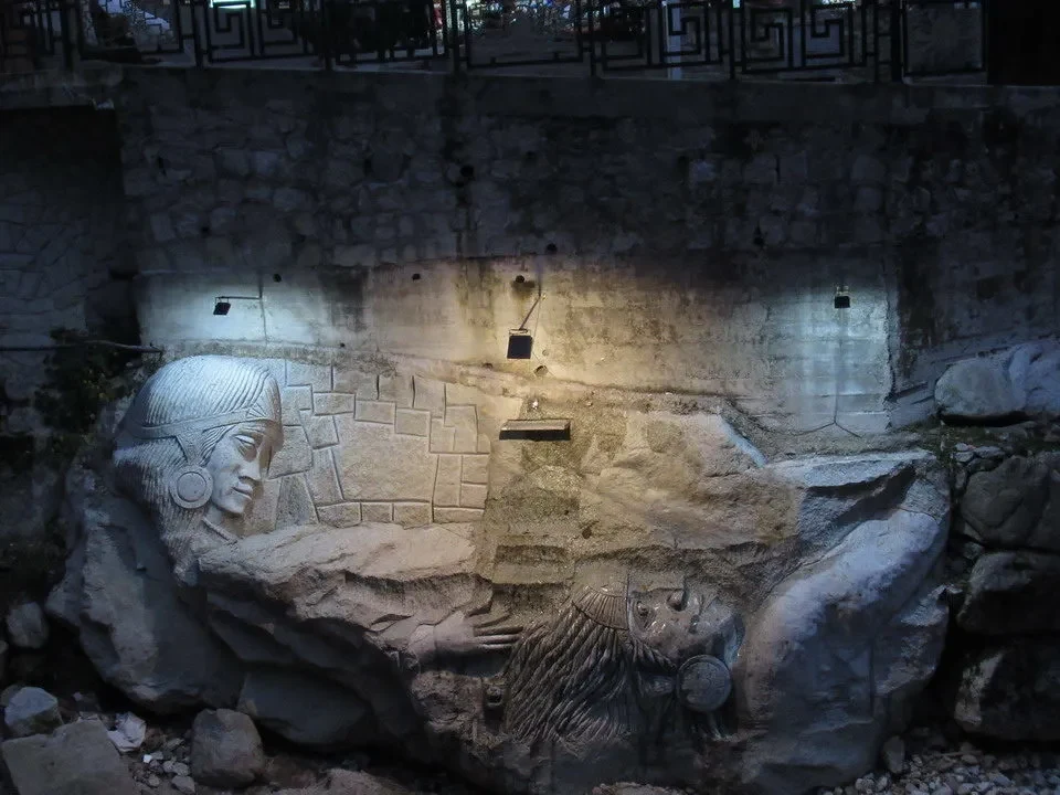 Rilievo scolpito di volti antichi incastonato nella roccia della parete.